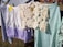 A series of clothes are hanging on a line. Included are a light purple and white skirt with lace detail, a piece of intricate beige crochet, a green checkered cloth, and a blue checkered fabric, all secured with clothespins. The background shows a grassy area with more people and structures.