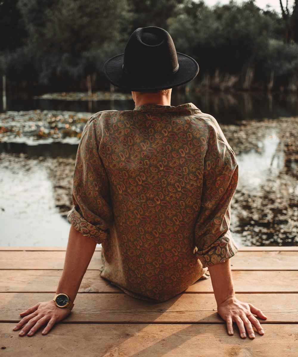 woman in brown long sleeve shirt and black hat sitting on brown wooden dock during daytime