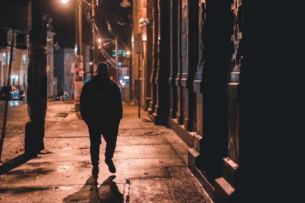 man in black hoodie walking on sidewalk during night time