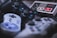 A collection of vintage and modern video game controllers includes devices from different gaming consoles. The controllers feature various buttons and joysticks, with some showcasing iconic buttons like the red and white buttons on an old Nintendo controller.