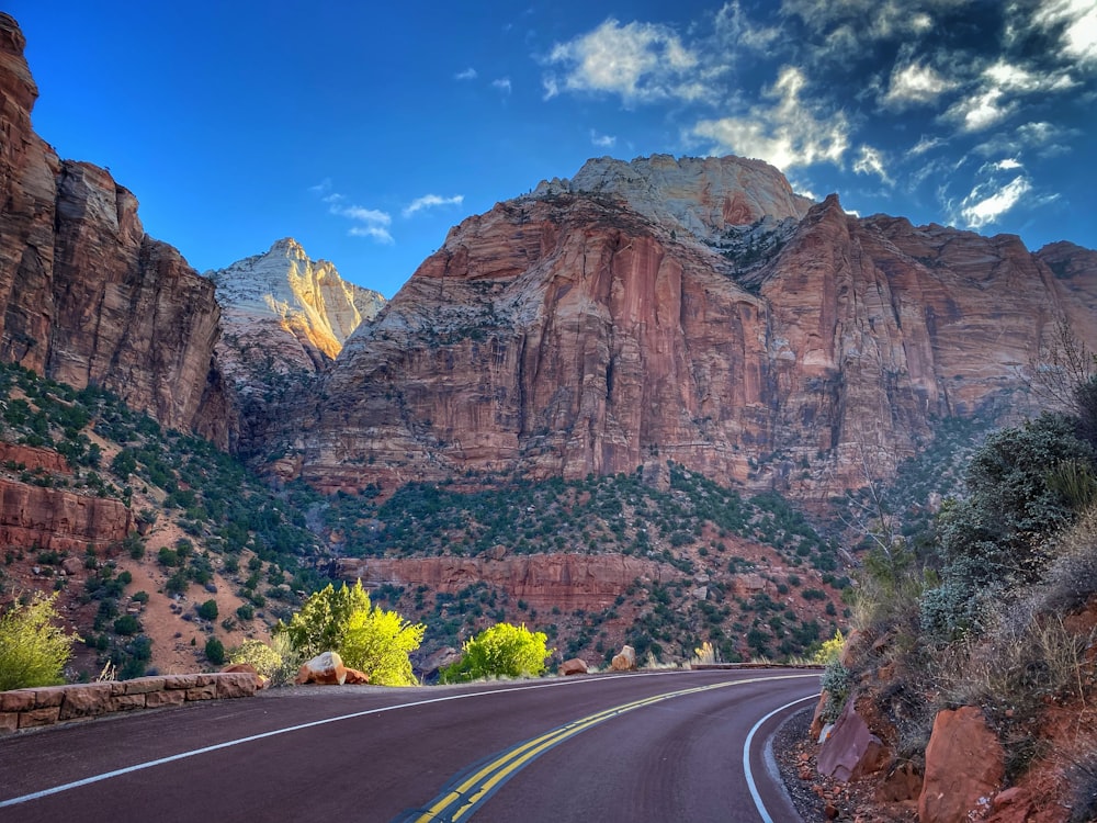 gray concrete road near brown rocky mountain under blue sky during daytime