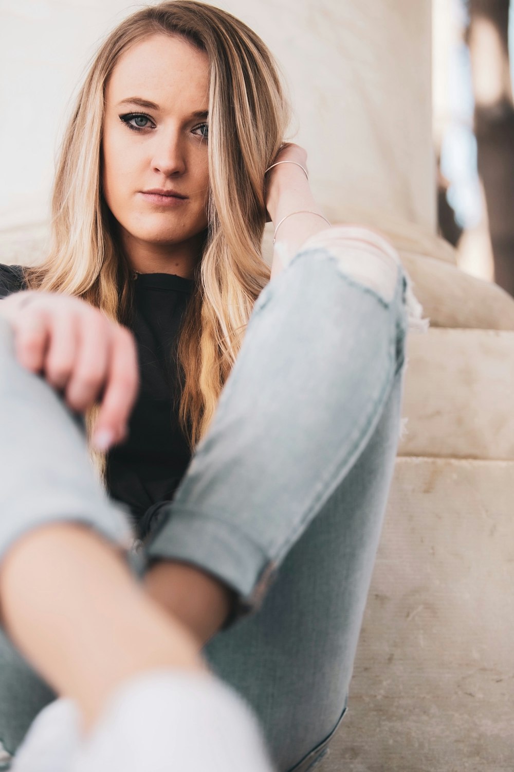 woman in black shirt and blue denim jeans sitting on brown concrete bench during daytime