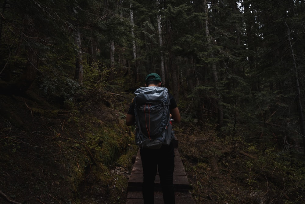 man in black pants carrying blue backpack walking on forest during daytime