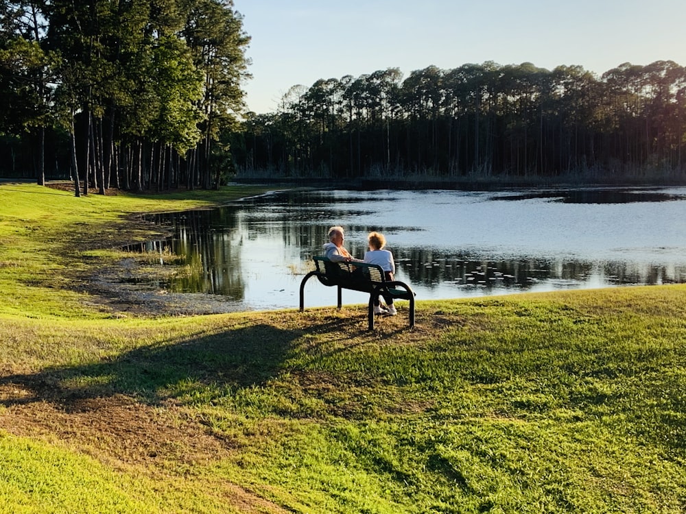2 person sitting on bench near lake during daytime