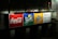 A brightly illuminated billboard displaying logos for Coca-Cola, Sprite, and Fanta. Each logo is prominently displayed against distinct colored backgrounds: red for Coca-Cola, green for Sprite, and orange for Fanta. To the right, there is text in Chinese. The surrounding environment appears dark and urban.