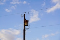 A utility pole with attached transformer and wires set against a clear blue sky with scattered clouds.