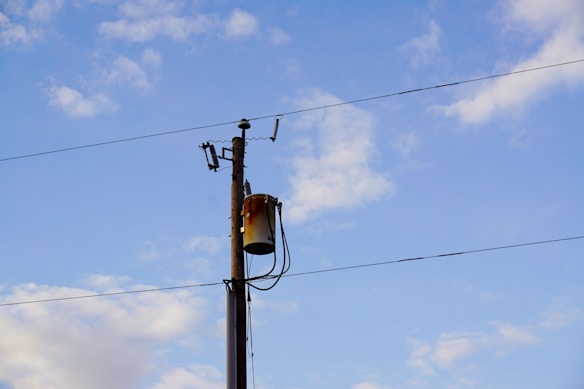 A utility pole with attached transformer and wires set against a clear blue sky with scattered clouds.