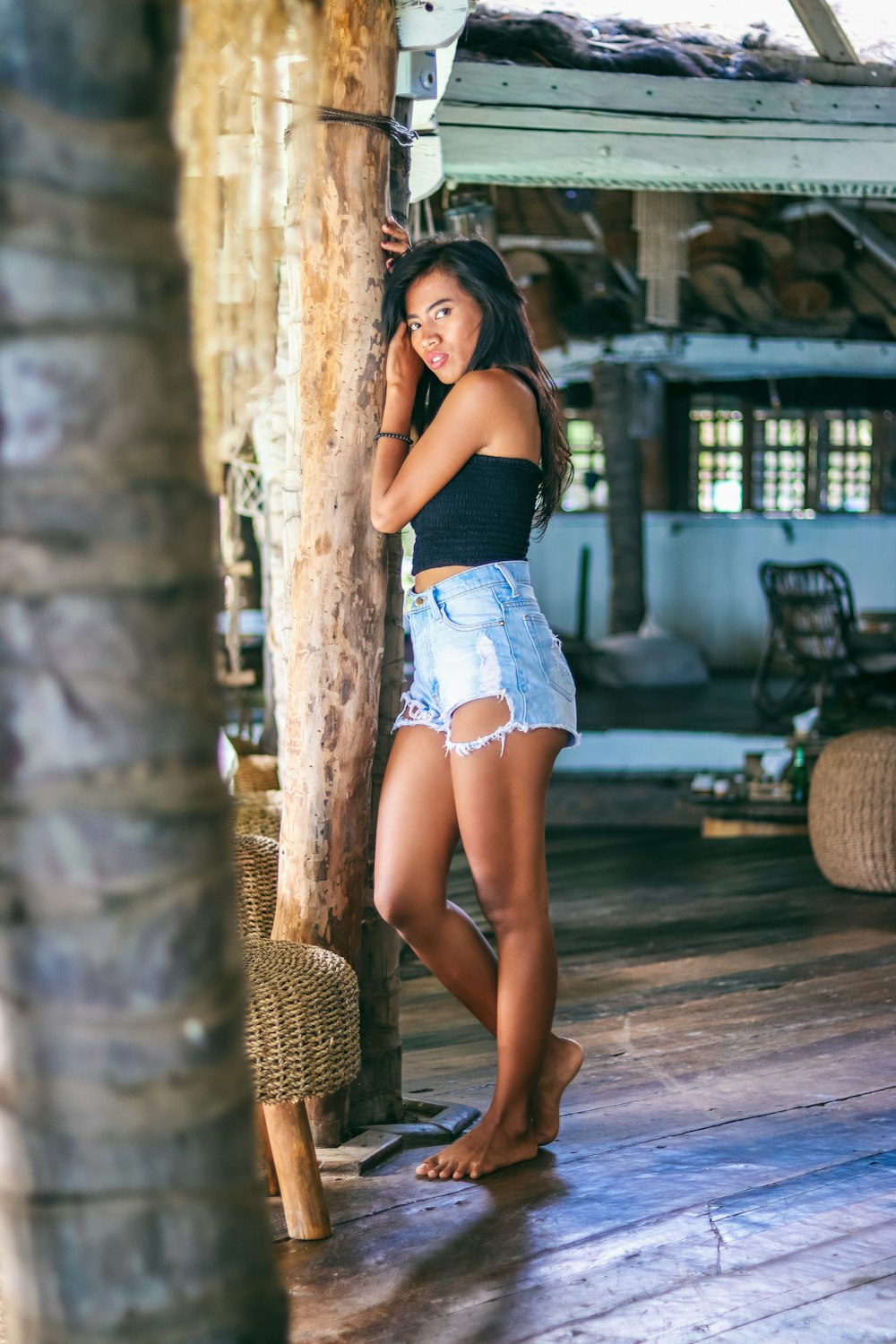 woman in black tank top and blue denim shorts leaning on brown concrete post during daytime