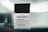 A sleek glass bottle of eau de parfum labeled 'DENVER Black.code 60 ml' with a black cap. The bottle is set against a soft, blurred background with a gradient of green and white tones, giving it an elegant and modern appearance.