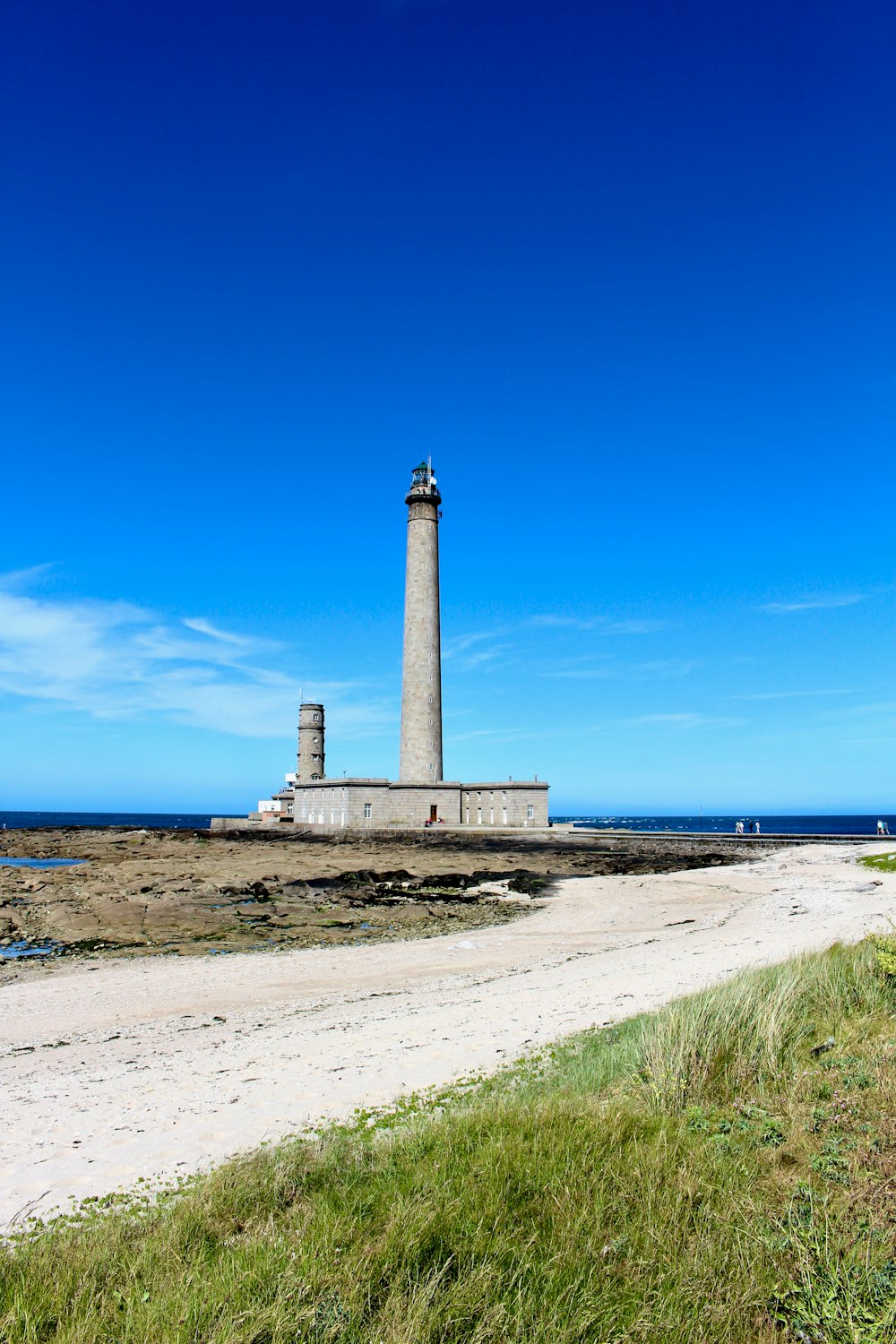 weißer und brauner Leuchtturm in der Nähe des blauen Meeres unter blauem Himmel tagsüber
