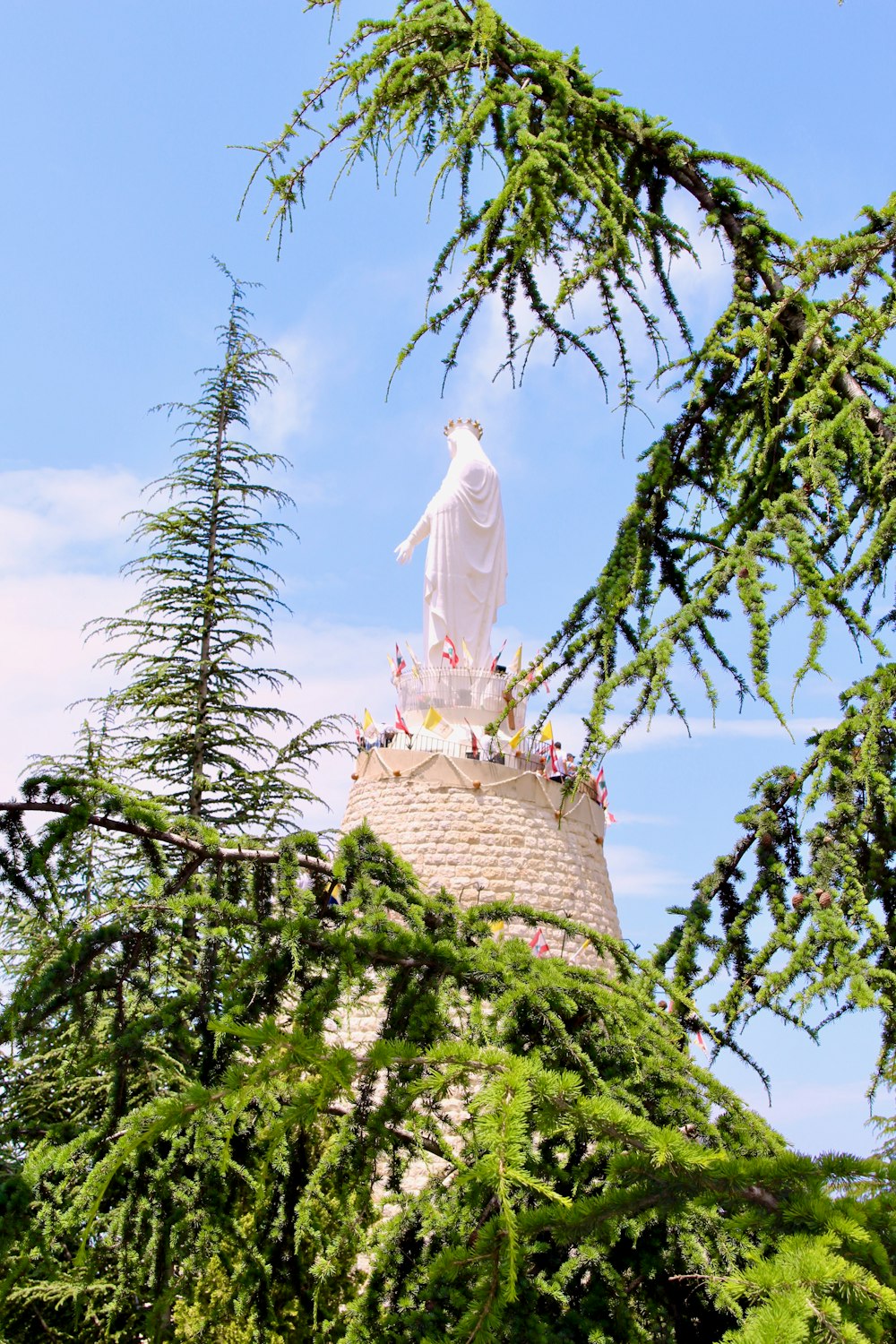 white statue on brown concrete tower near green trees during daytime