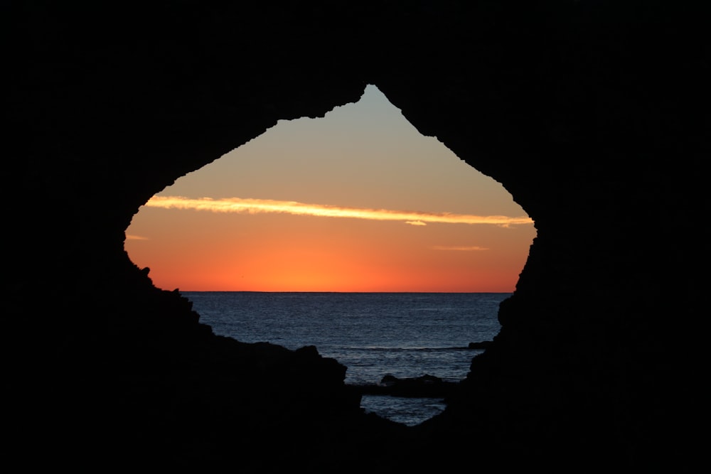 the sun is setting over the ocean from a cave