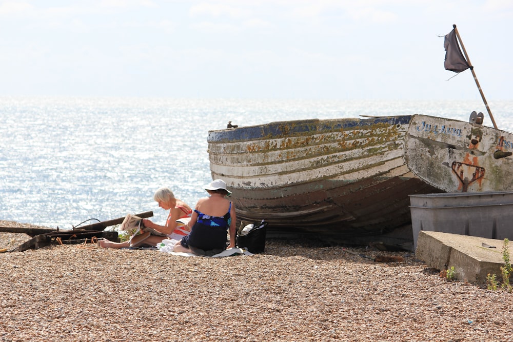 2 boys sitting on brown wooden boat on beach during daytime