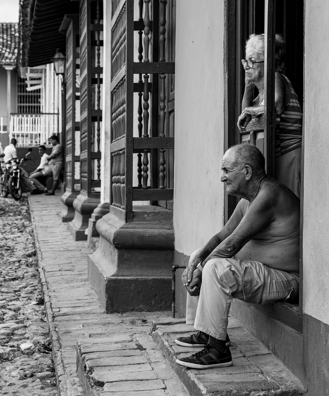 grayscale photo of man sitting on concrete bench