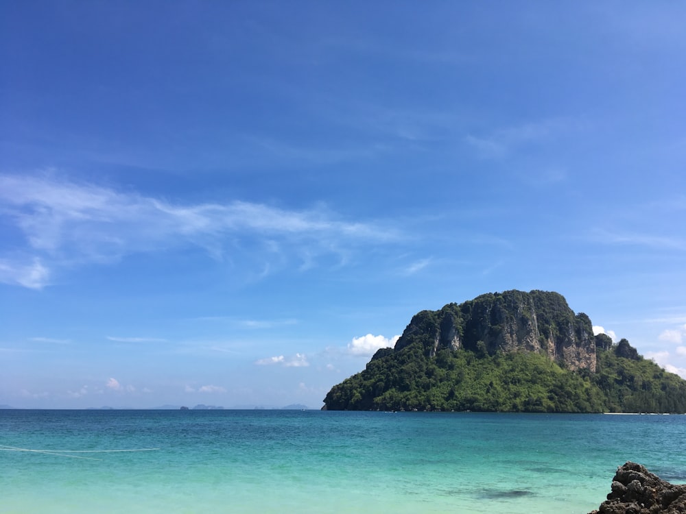 green and brown rock formation on sea under blue and white cloudy sky during daytime