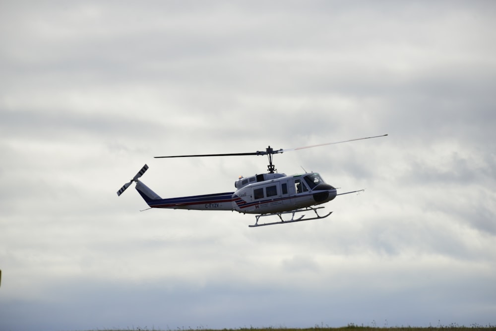 white and black helicopter flying under white clouds during daytime