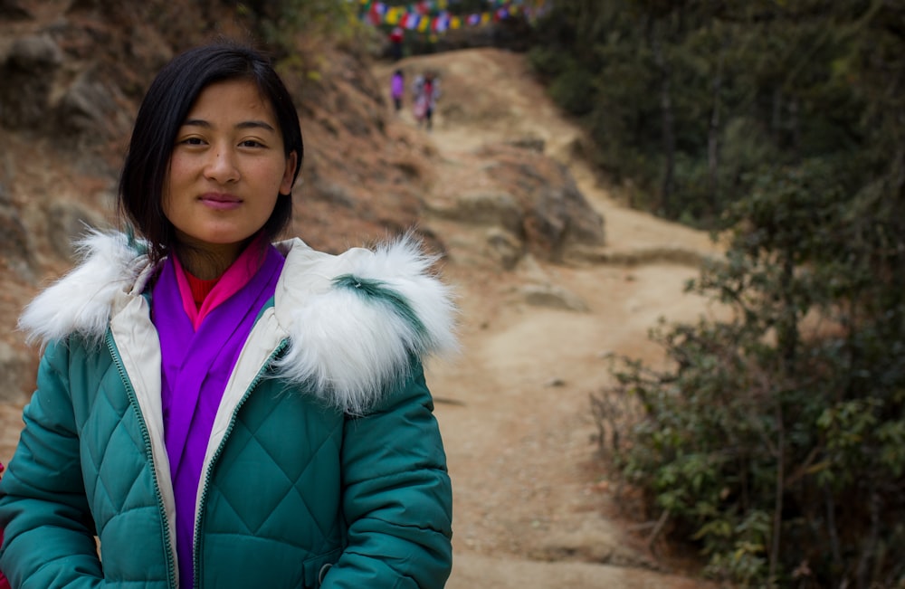 woman in green jacket standing near brown rock