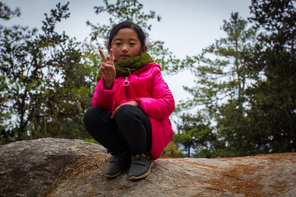 girl in green jacket sitting on brown rock during daytime