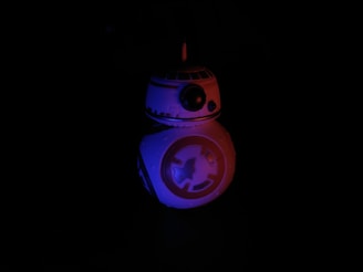 A spherical, futuristic droid illuminated with blue and red lights stands against a black background. The droid has a domed head with antenna-like protrusions and a circular body marked with tech-inspired designs.
