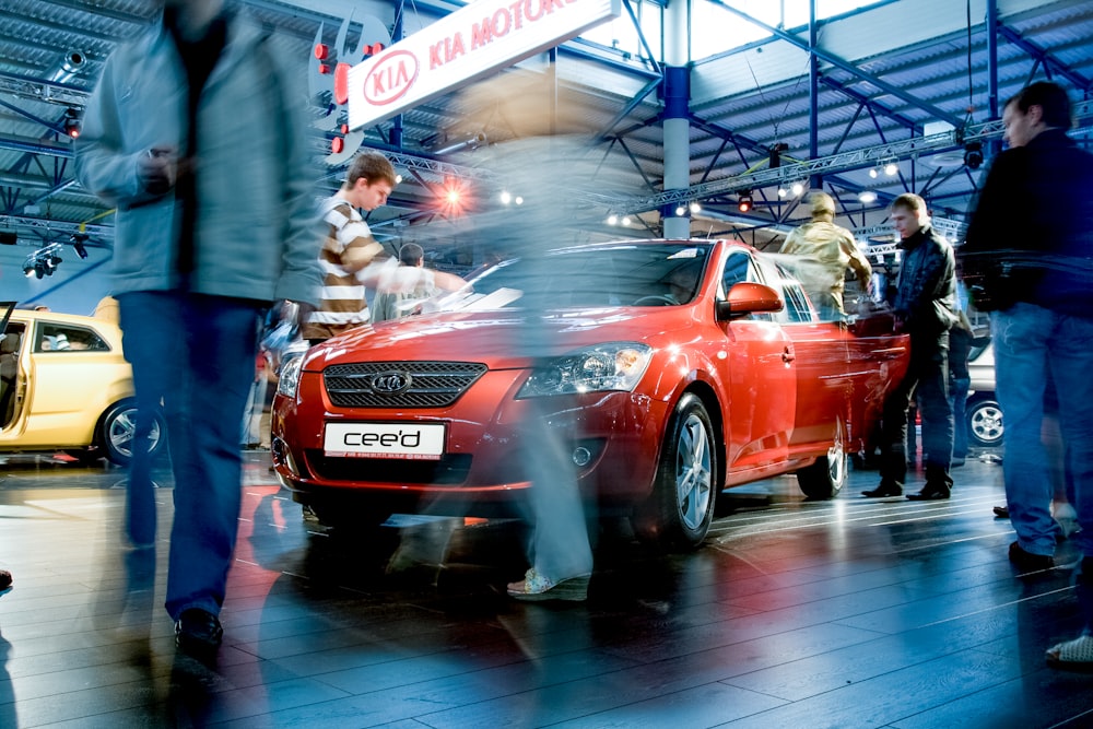 man in black jacket standing beside red car