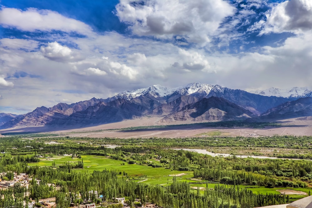 green grass field near mountain under white clouds during daytime