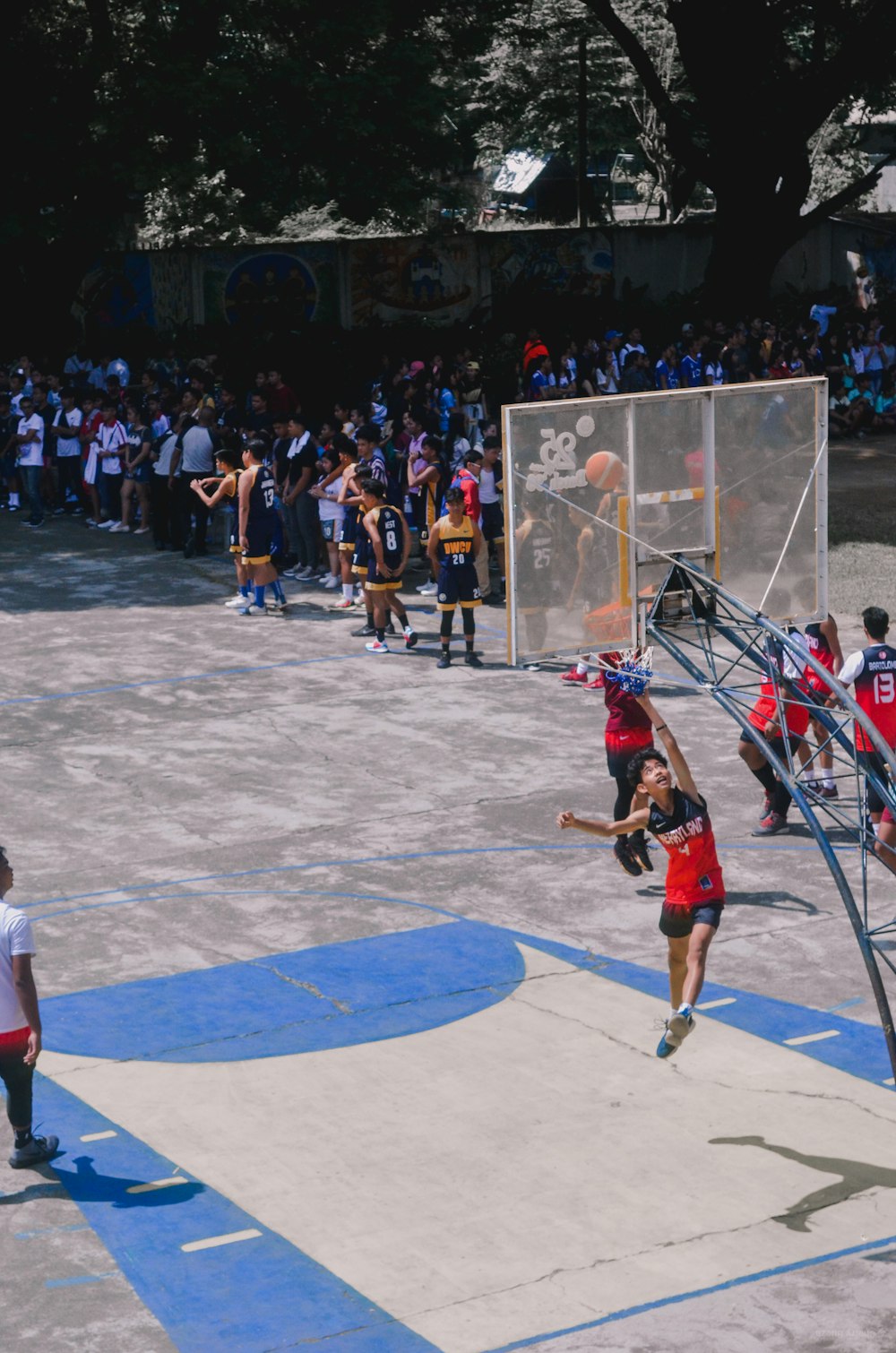 man in red jersey shirt and blue shorts standing on basketball court