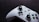 A white gaming controller with black buttons and colorful accents, including green, red, yellow, and blue buttons, is placed on a dark, textured surface. The design features dual analog sticks, a directional pad, and various control buttons, some labeled with letters.