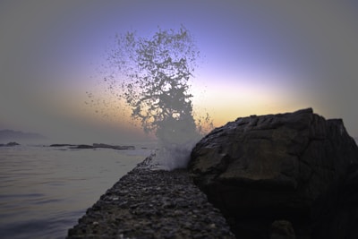 Waves crashing against ancient stones under a twilight sky with hints of green and blue.