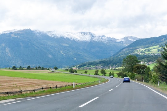 black car on road near green grass field and green mountains during daytime in Land Salzburg Austria