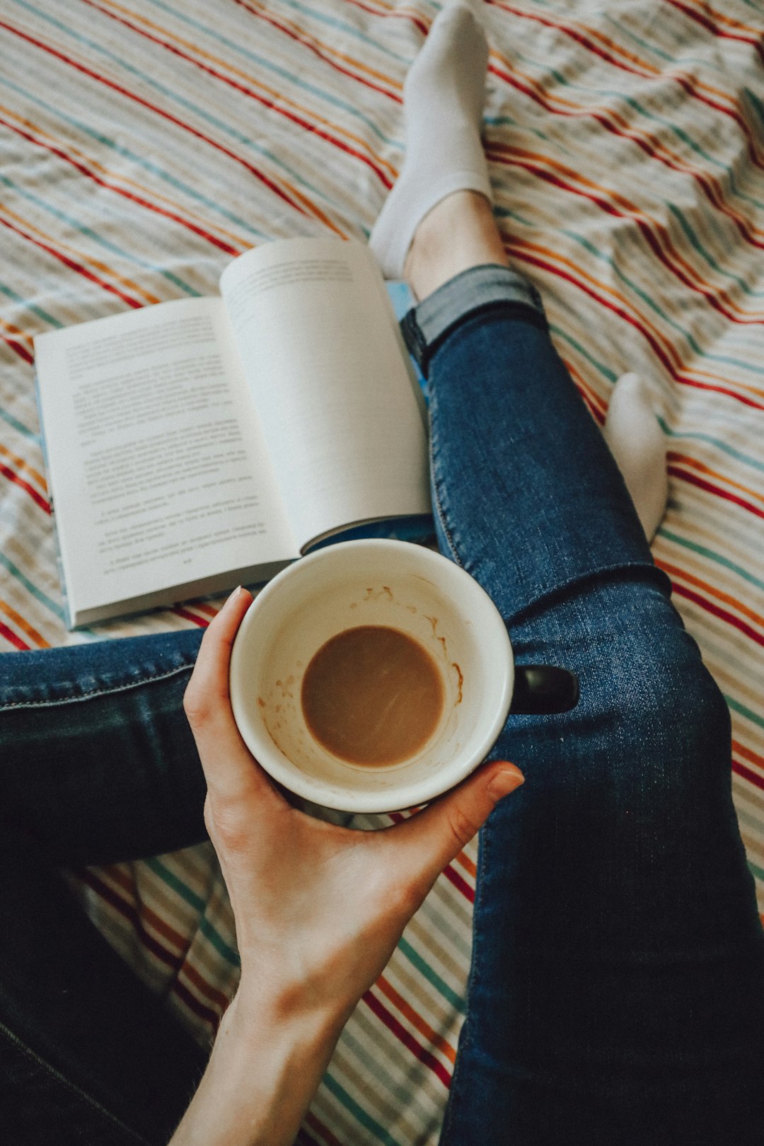 person in blue denim jeans holding white ceramic mug