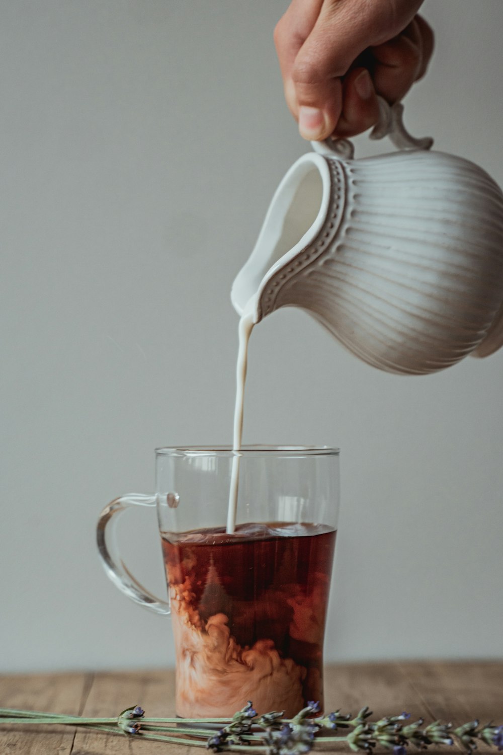 white ceramic teapot pouring red liquid on clear glass mug