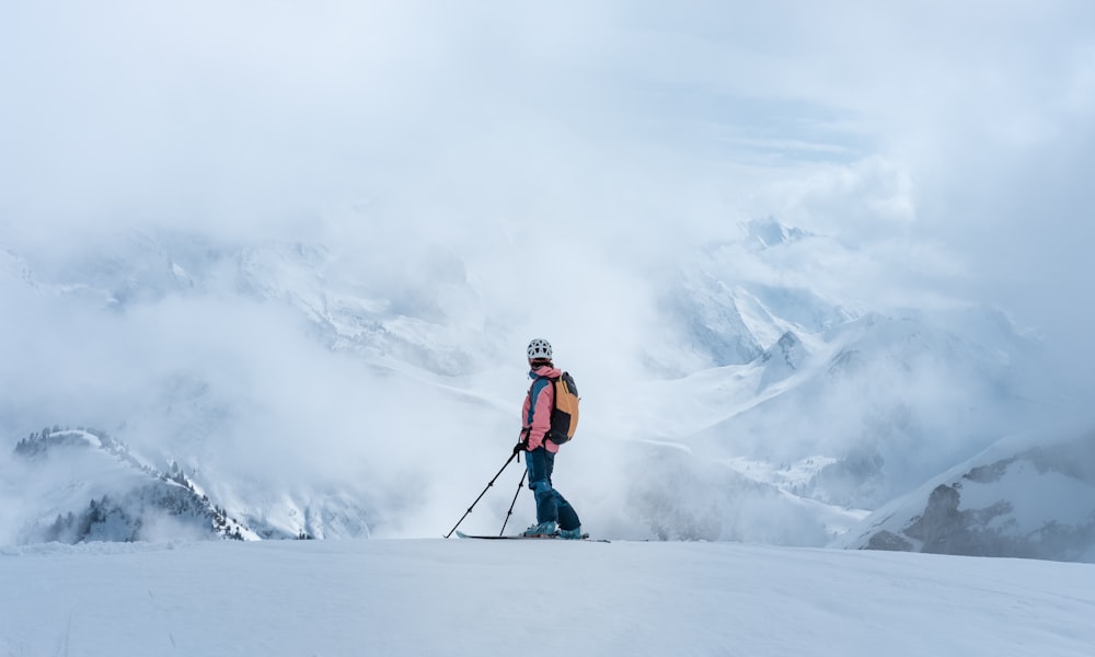 man in orange jacket and black pants standing on snow covered ground