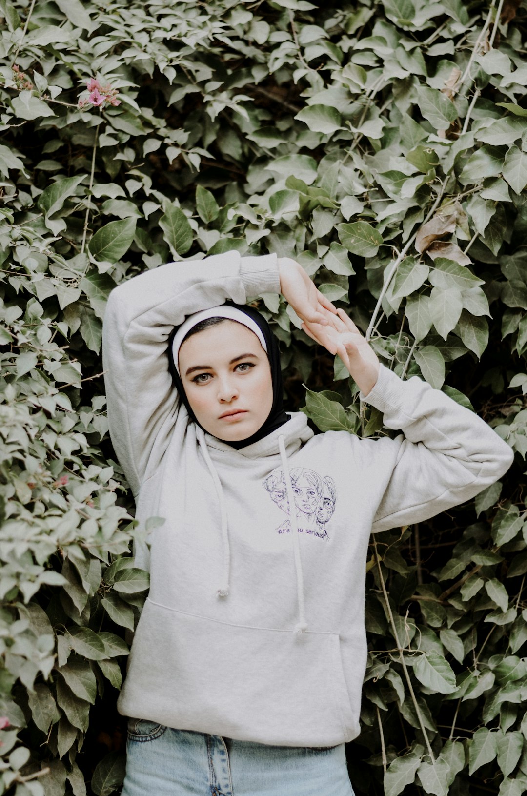 woman in white hoodie standing beside green plant
