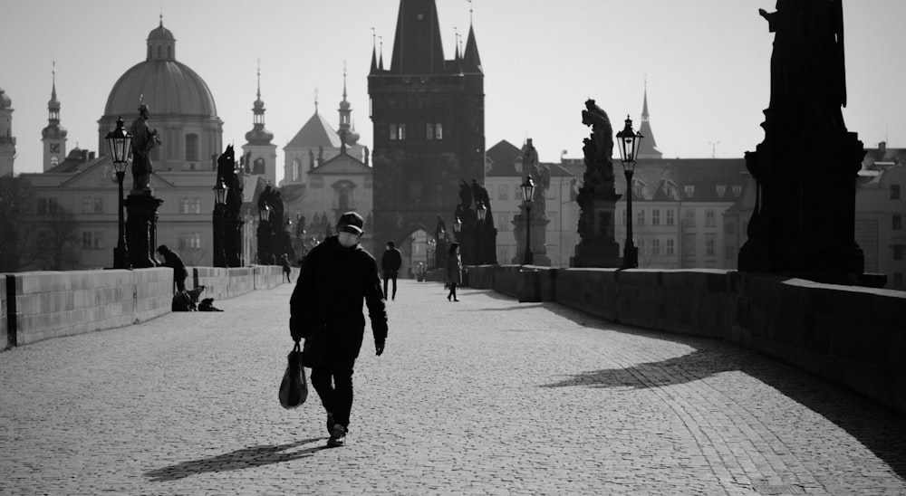 man in black jacket and pants walking on sidewalk in grayscale photography