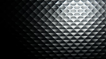 The image features a close-up view of a textured surface with a diamond pattern. The surface appears metallic and reflects light, creating varying shades of gray and black across the pattern.