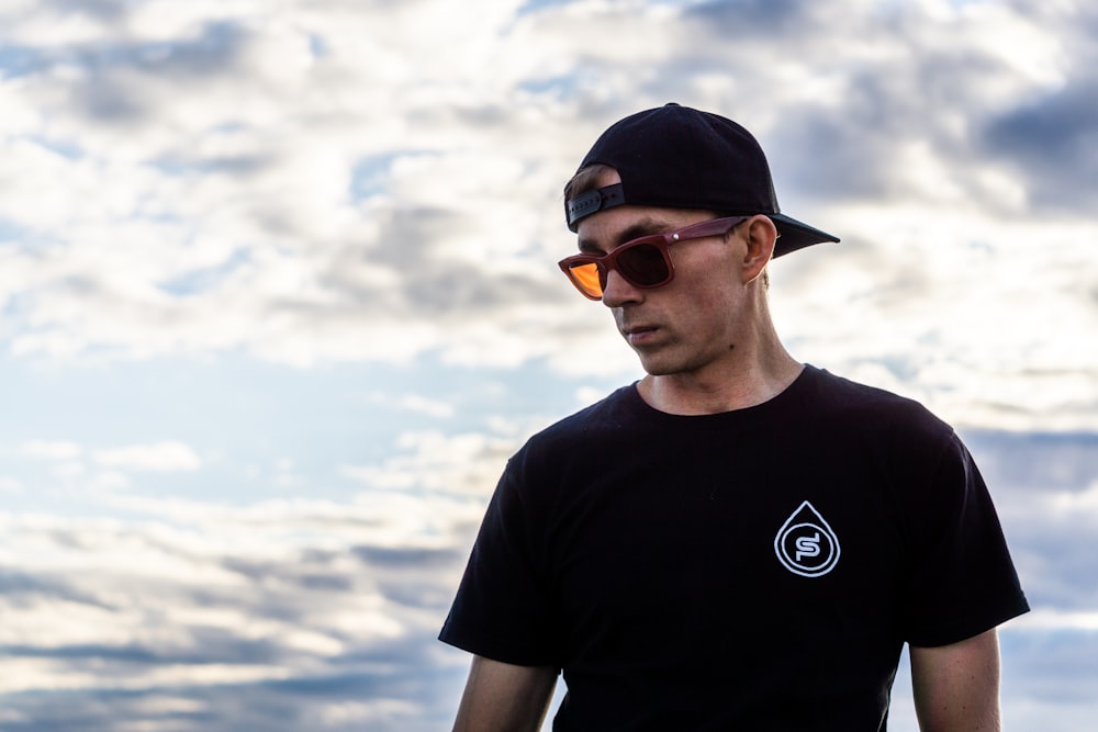 man in black crew neck t-shirt wearing orange sunglasses and black cap