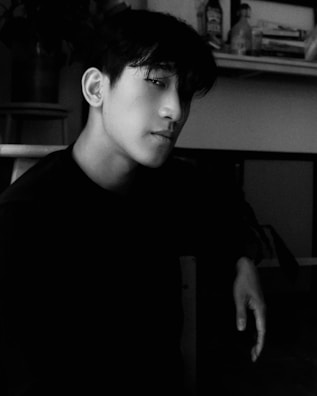 Black and white portrait of jax rowe seated with a contemplative expression, surrounded by books.