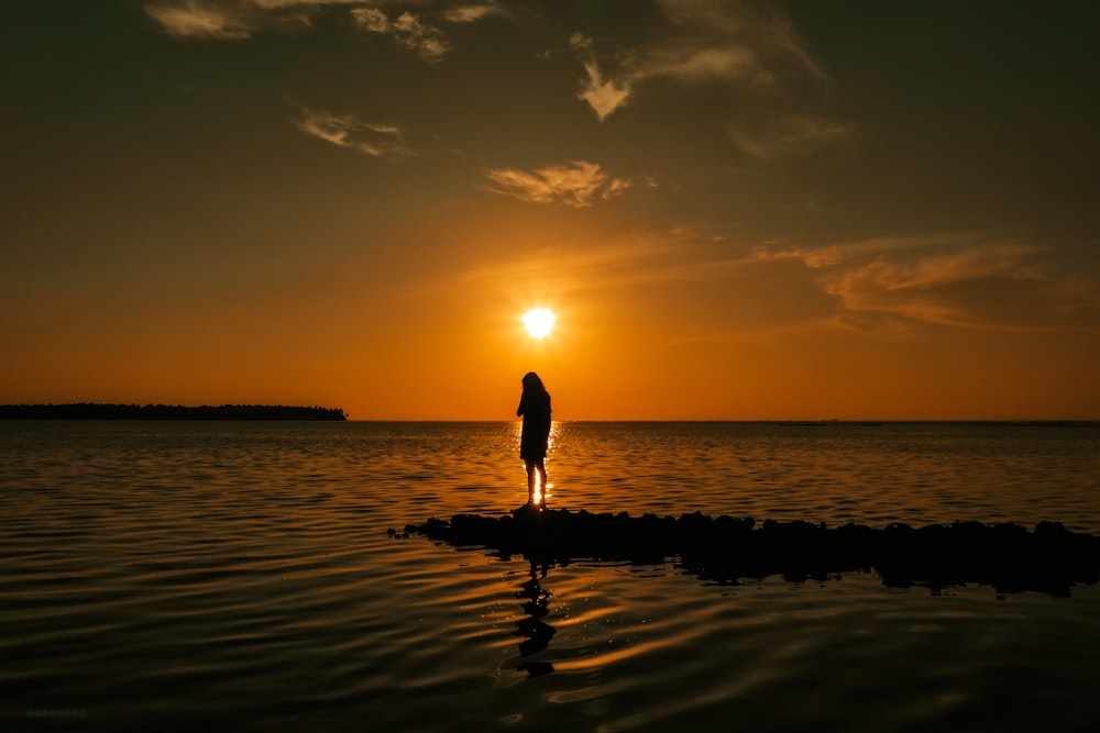 silhouette of woman walking on beach during sunset