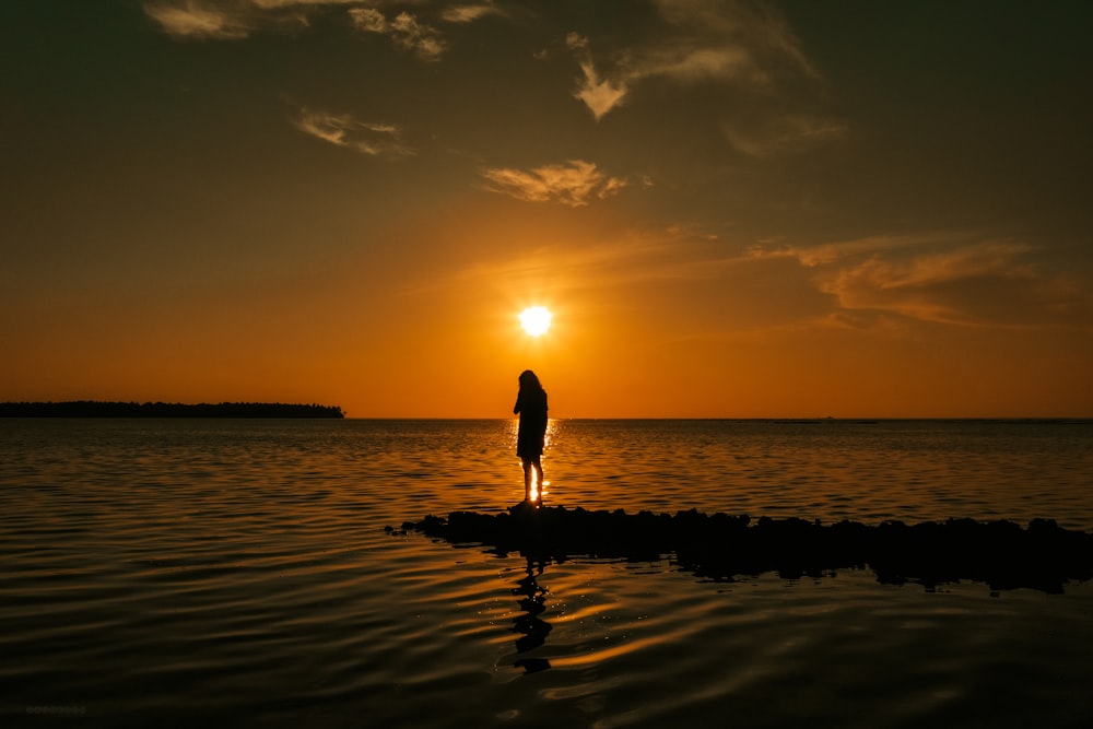 Silhouette einer Frau, die während des Sonnenuntergangs am Strand spazieren geht