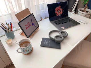 A warm, inviting desk setup with a notebook, pen, and a cup of tea beside a laptop showing an email inbox.