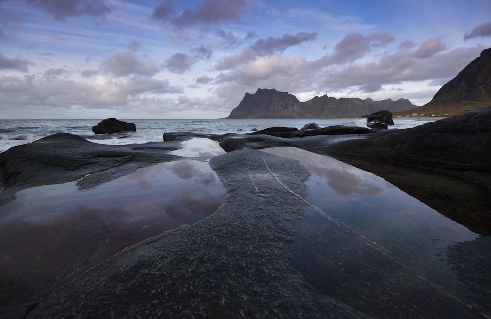 body of water near mountain under cloudy sky during daytime