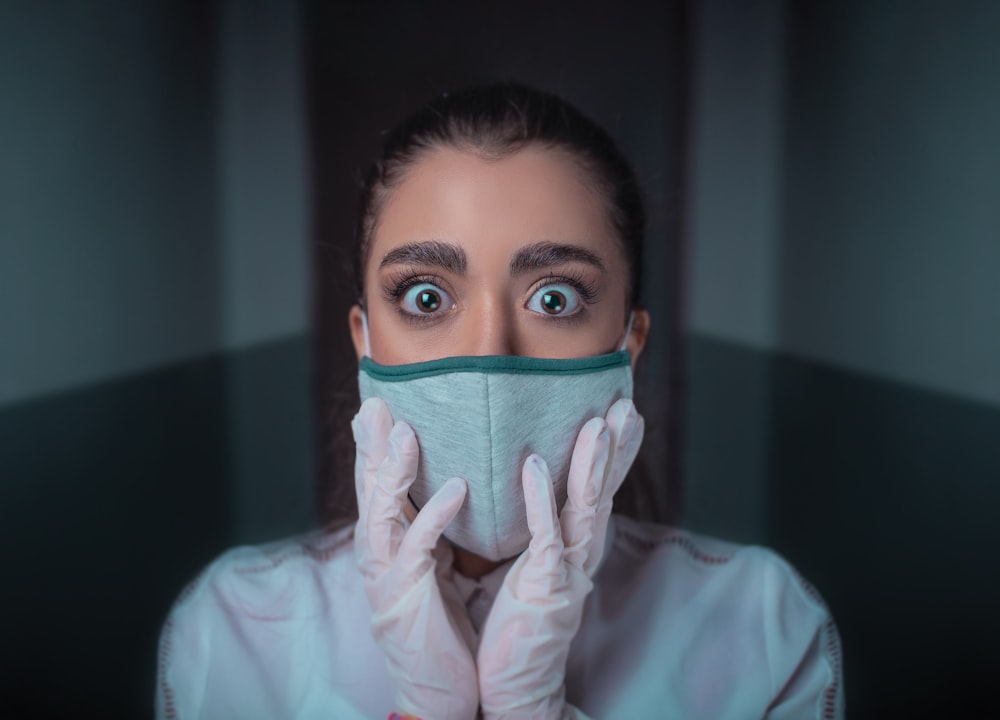 woman in white long sleeve shirt covering her face with blue and black face mask