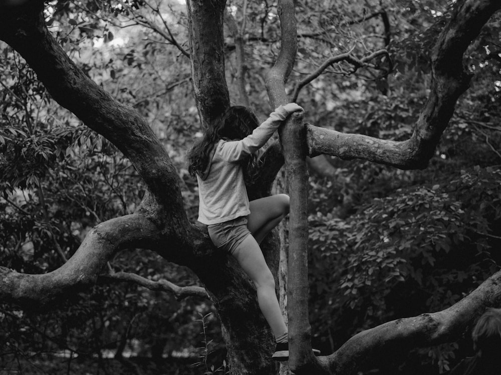grayscale photo of woman in white t-shirt and shorts sitting on tree branch
