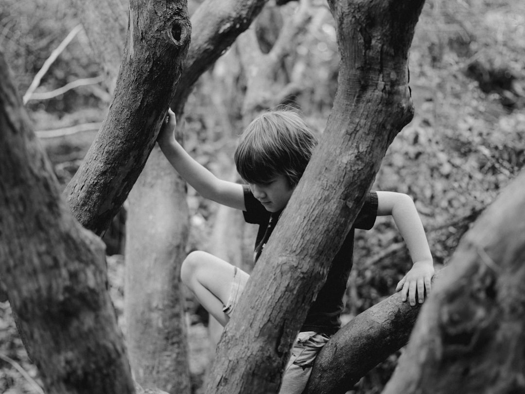 grayscale photo of woman in black tank top climbing on tree