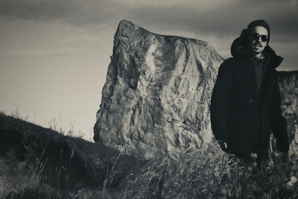 person in black hoodie standing on grass field near rocky mountain during daytime