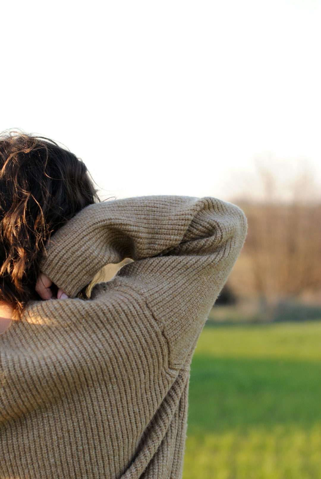 woman in gray sweater sitting on green grass field during daytime