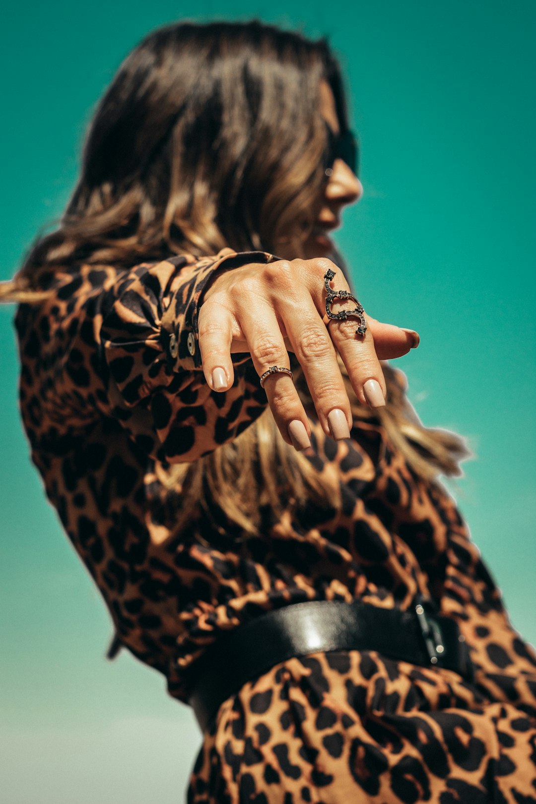 woman in black and brown leopard print long sleeve shirt covering her face with her hands