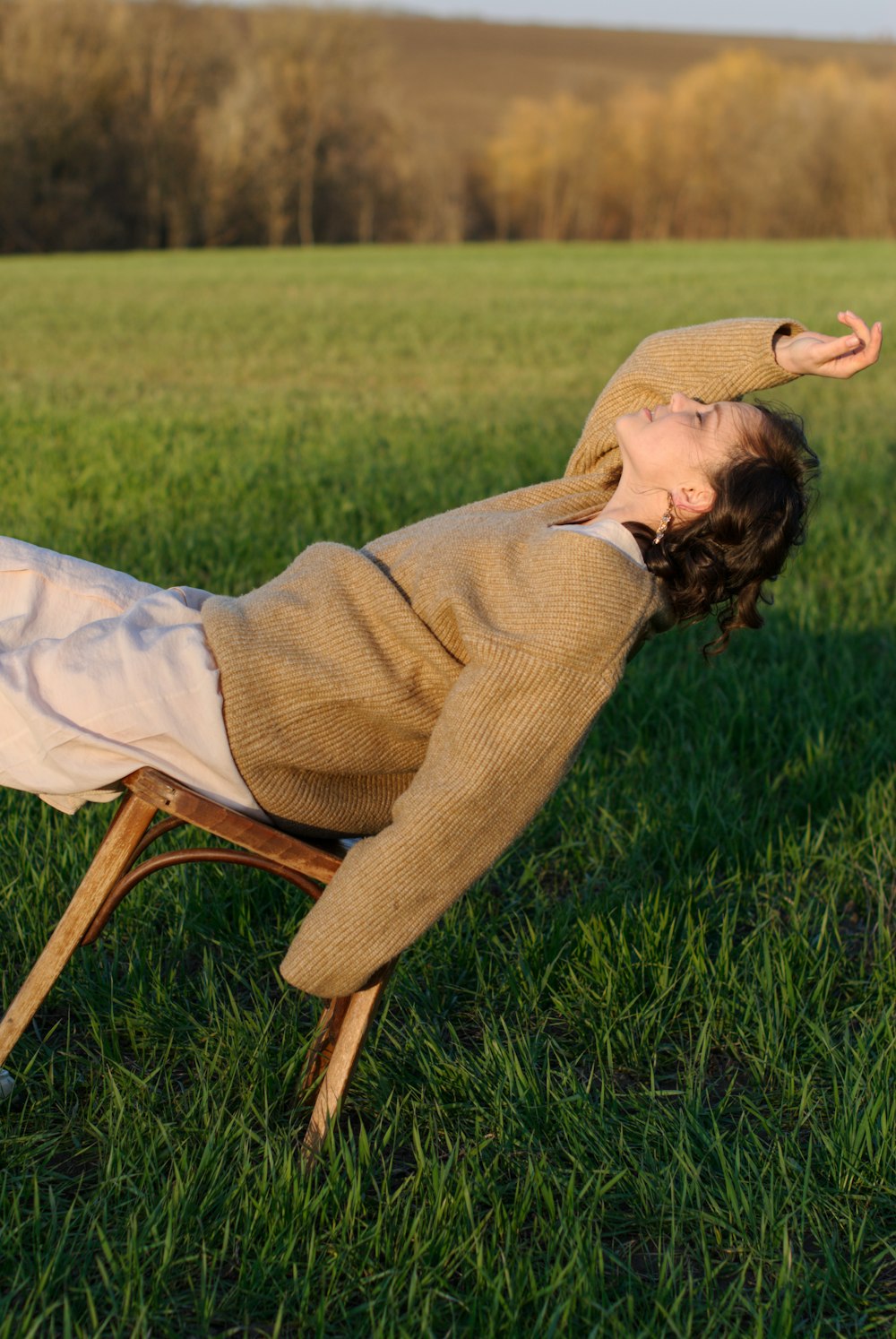 woman in brown cardigan and blue denim jeans sitting on brown wooden chair on green grass