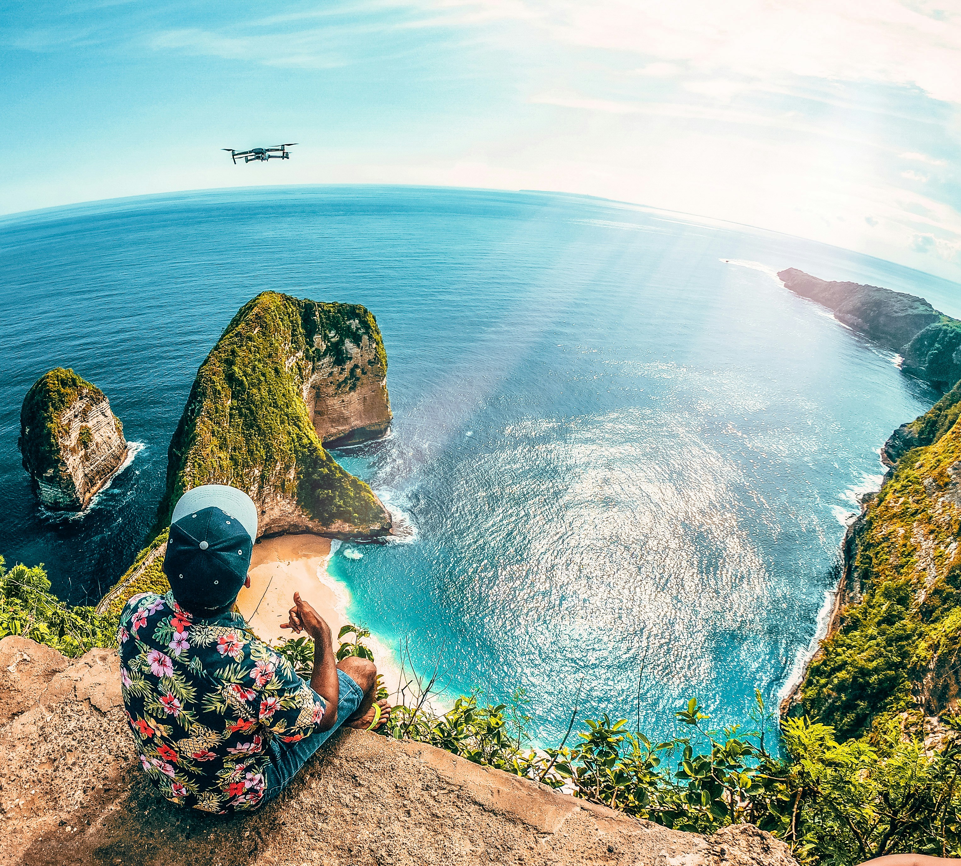 woman in blue and white floral dress sitting on rock formation near body of water during