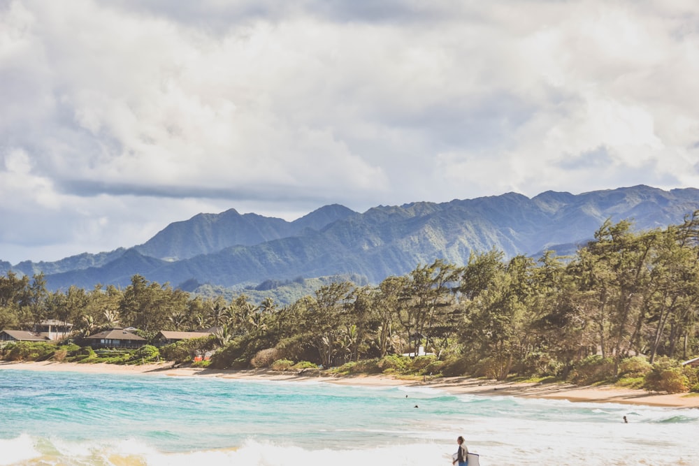 person in beach near mountain under white clouds during daytime